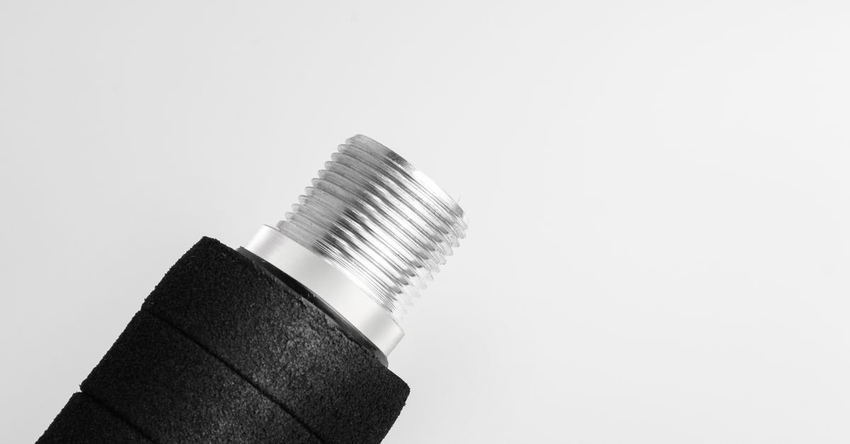 Macro photograph of a machined metallic industrial connector showing its central stem and threaded collar