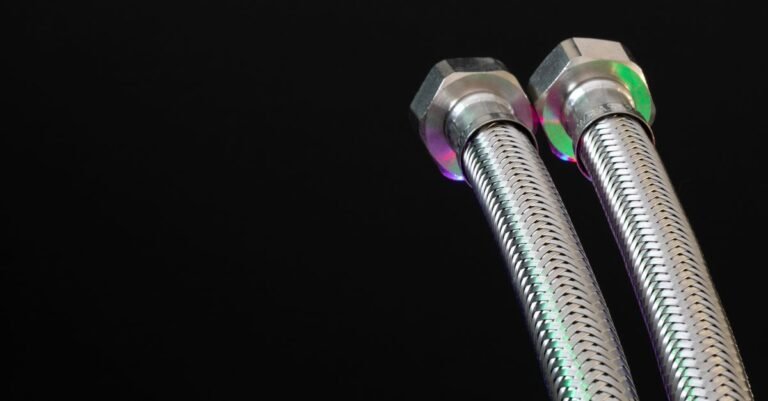 Close-up of braided metal flex hoses with threaded hex nut fittings on a dark background