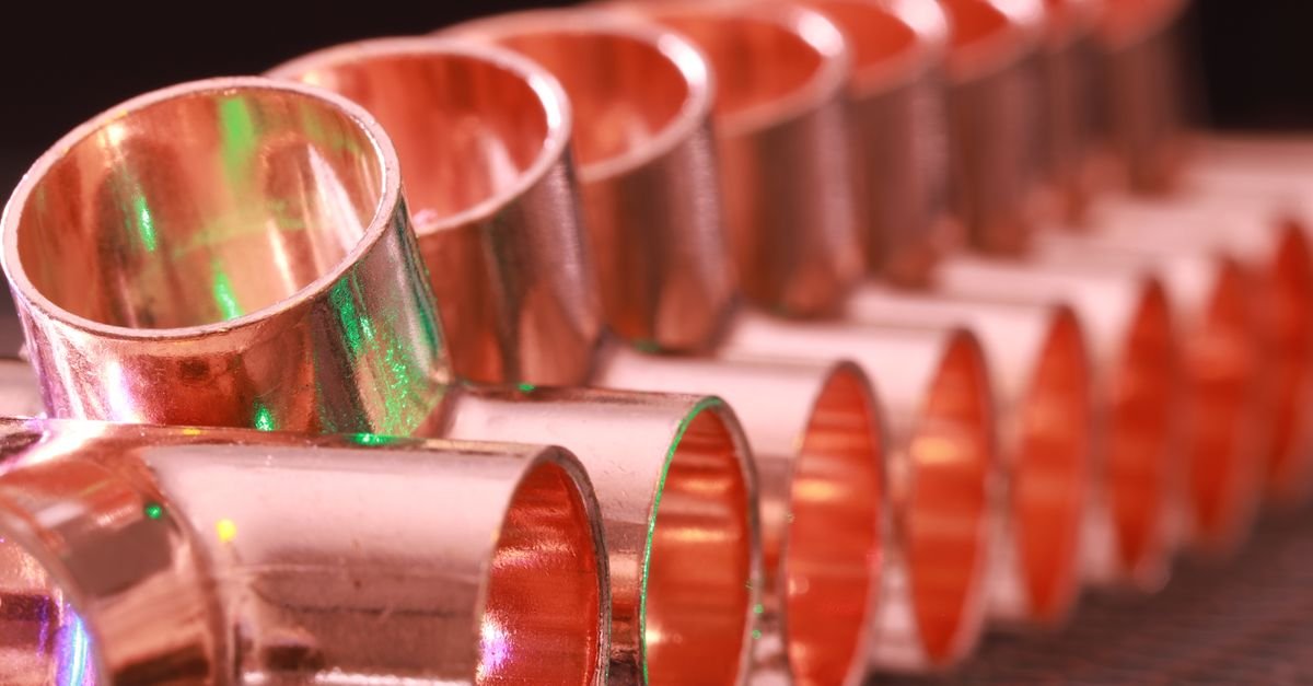 Copper plumbing fittings of several shapes arranged in a row on a plain surface