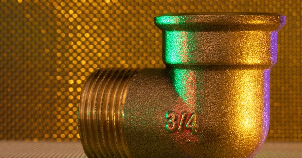 A polished three-quarter-inch brass pipe fitting photographed against a warm textured background