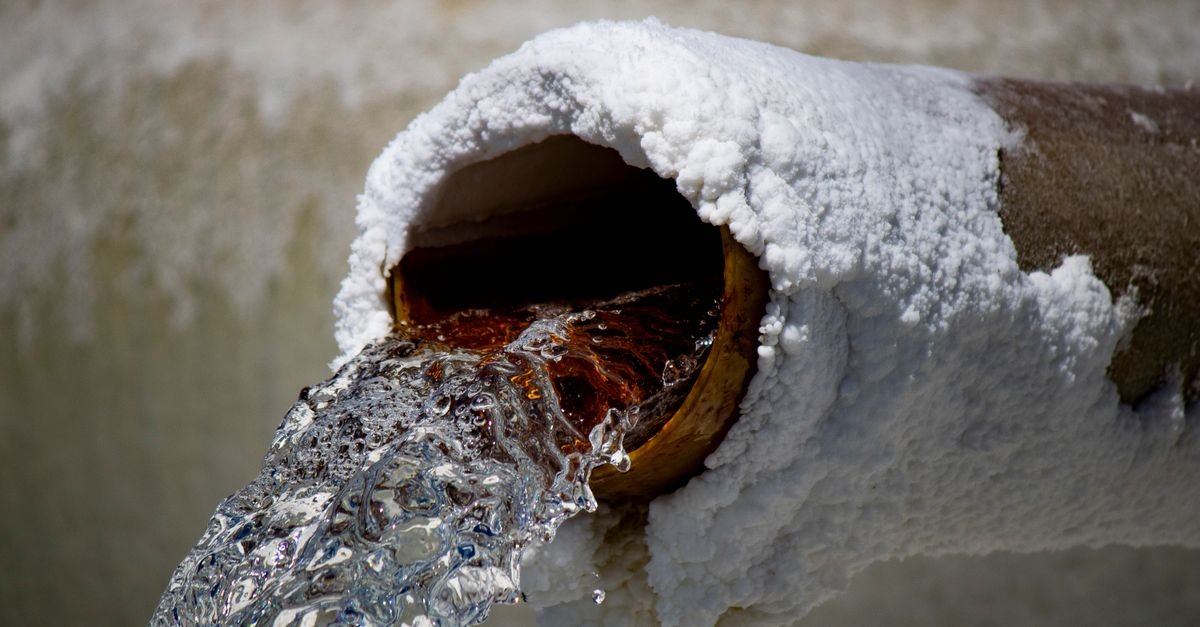 Water running from a corroded pipe with mineral deposits crusted around the outlet, the sort of debris a pressure washer inlet filter is holding back
