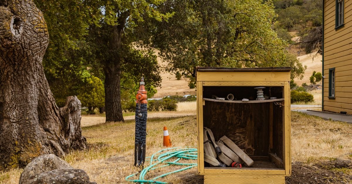 Garden hoses lying outdoors in full summer sun beside a utility box, where wall temperature and softening are highest