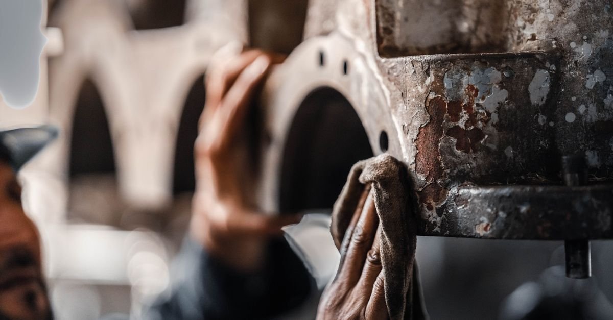 Worker cleaning corroded metal machinery during routine maintenance