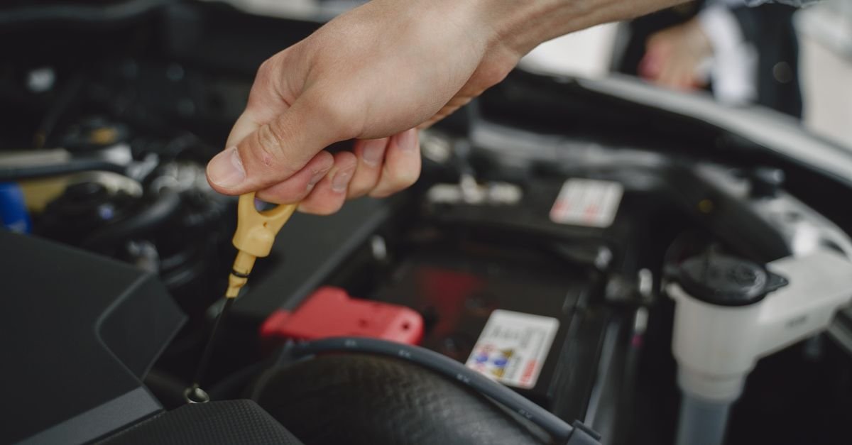 A hand checking an oil dipstick in an engine bay to read the level against the marks