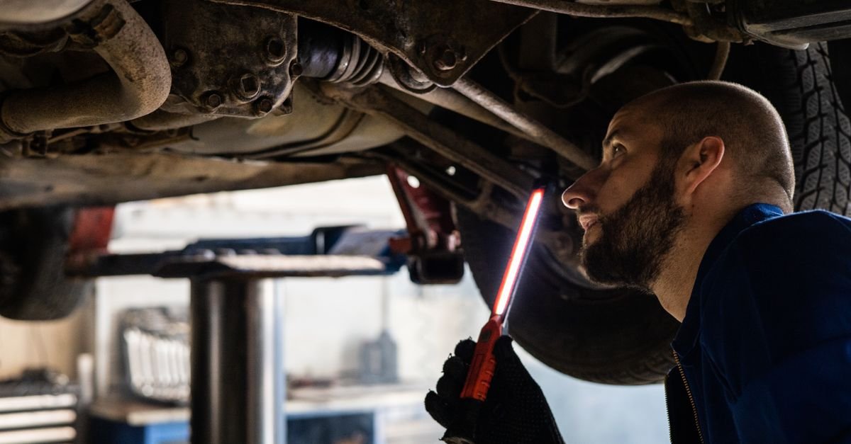 A technician using a work light to inspect the underside of a machine for the source of a leak