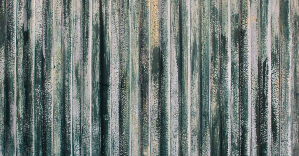 Weathered green and white painted corrugated metal with dark vertical stripes running down it