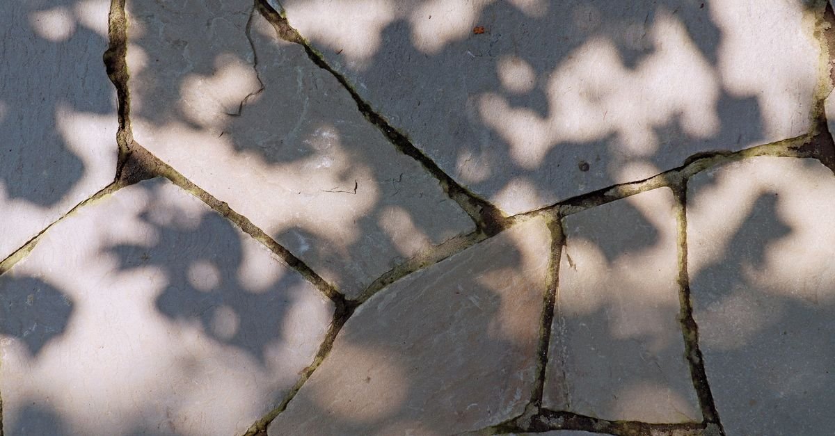 Low sunlight raking across cracked stone paving and throwing the surface texture into relief