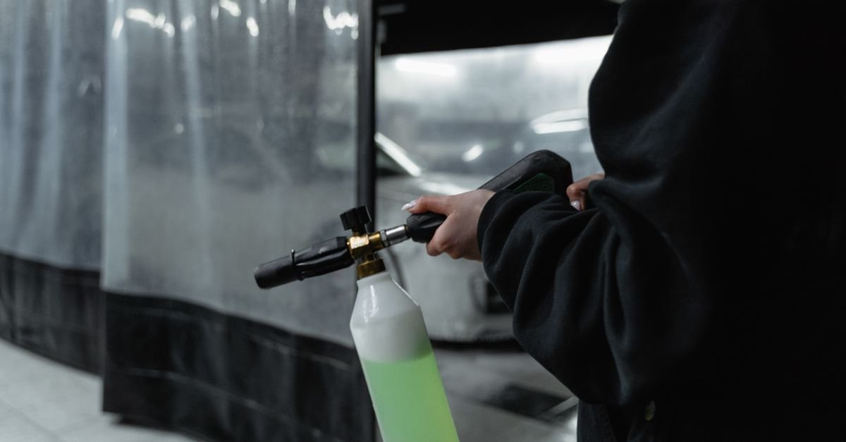 Close-up of a spray gun and nozzle assembly held in a garage cleaning bay