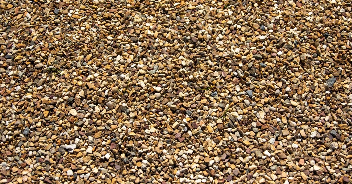 Close-up of loose grey gravel showing rough granular texture, the exact sound people describe when a pressure washer pump is starving for water