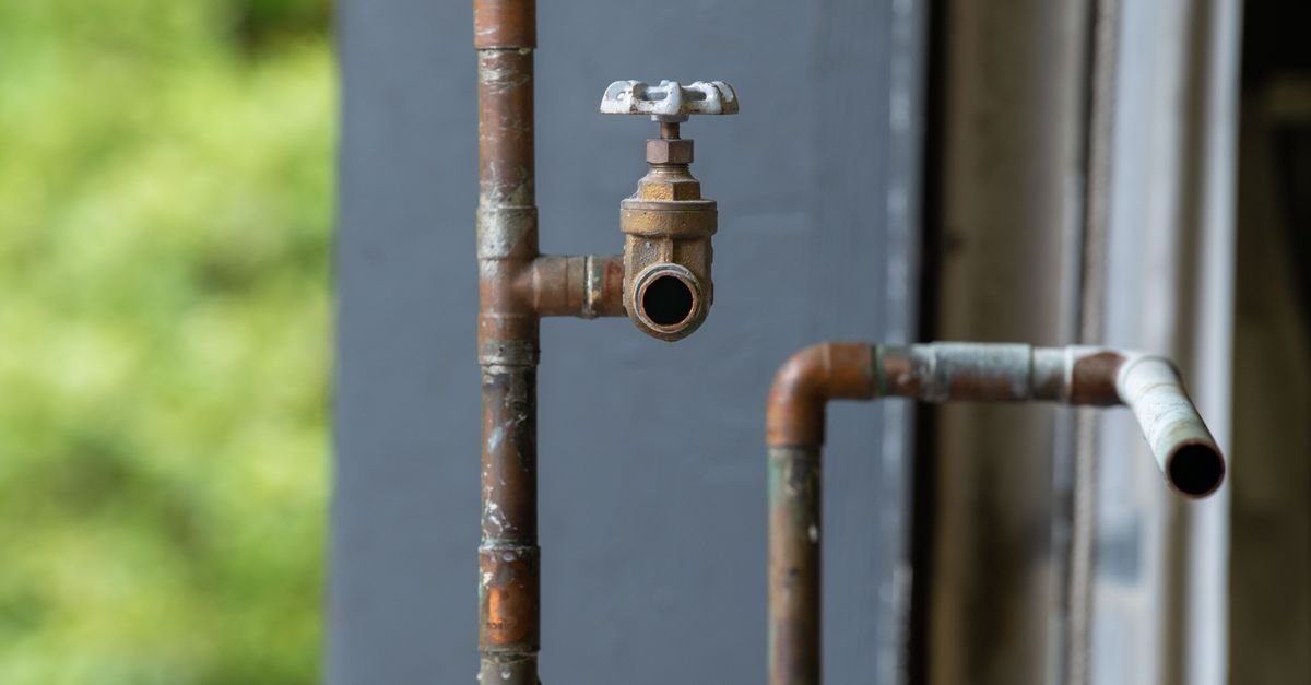 An old rusted industrial water pipe with a valve, the kind of corroded supply line that halves flow while static pressure still reads normal