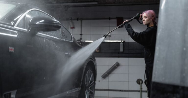 Operator gripping a pressure washer trigger gun and wand while rinsing foam from a black car