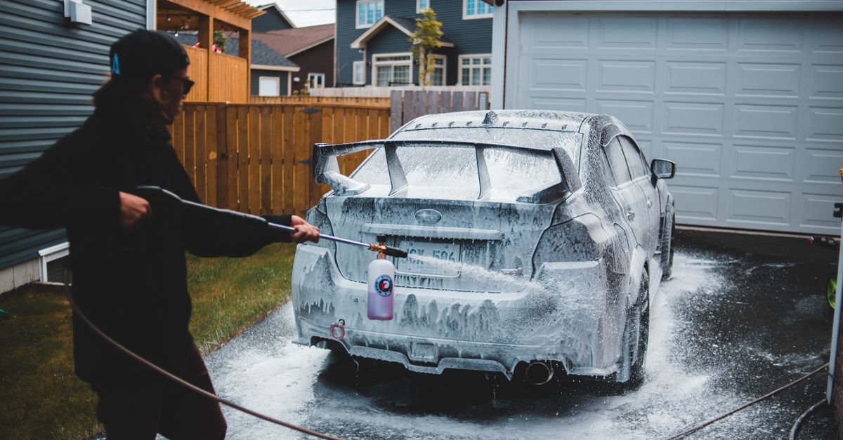 Homeowner using a pressure washer foam attachment on a car in a residential driveway