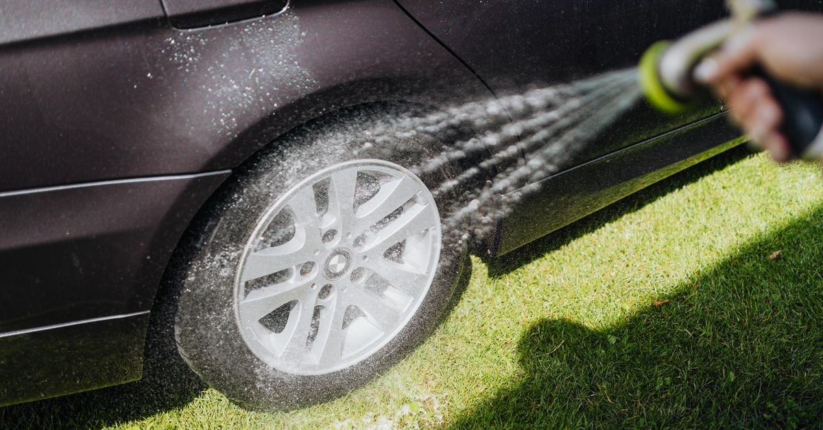 Close-up of a car wheel rim being rinsed with a fan spray of water