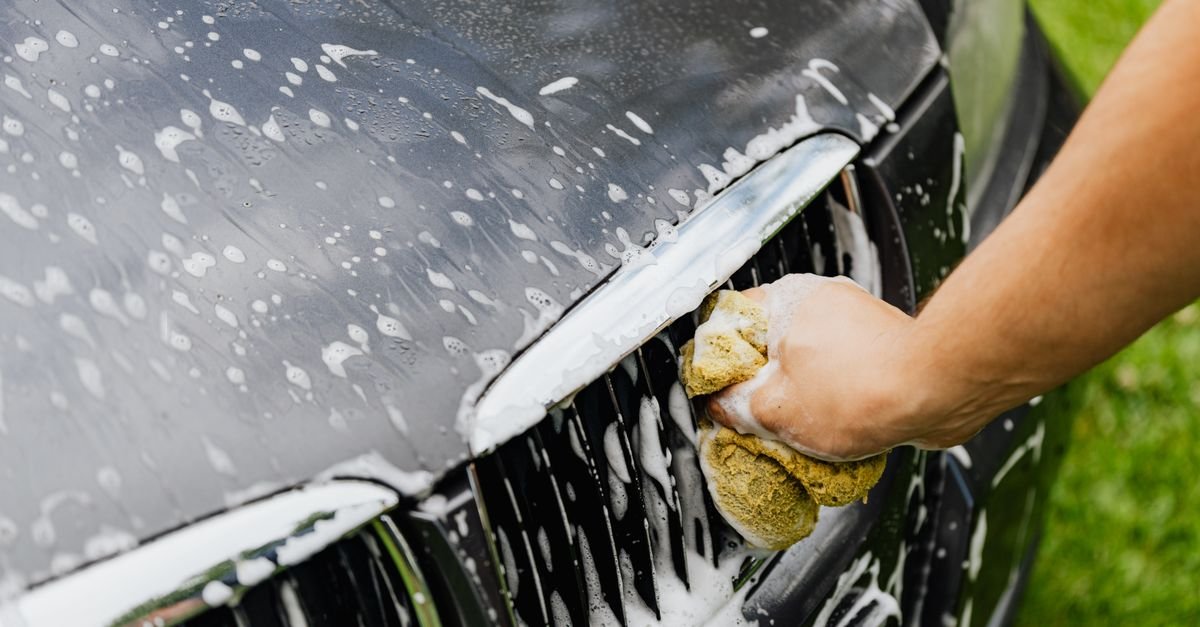 A hand cleaning a car grille by hand with a soapy sponge