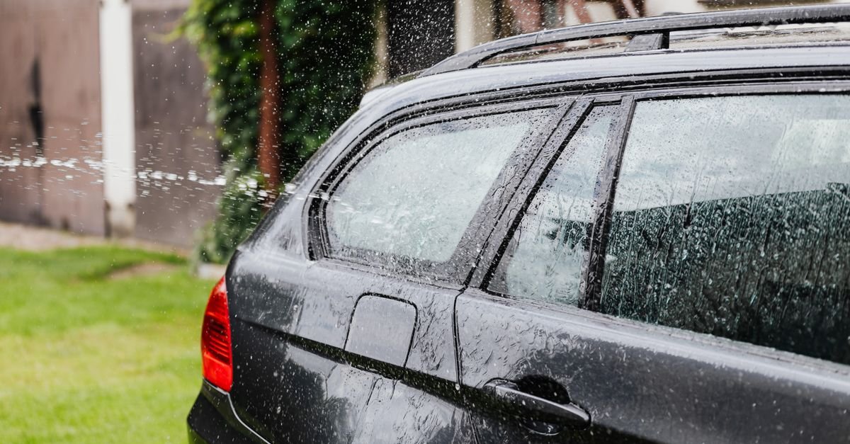 Side view of a black car being rinsed with a wide fan of water outdoors
