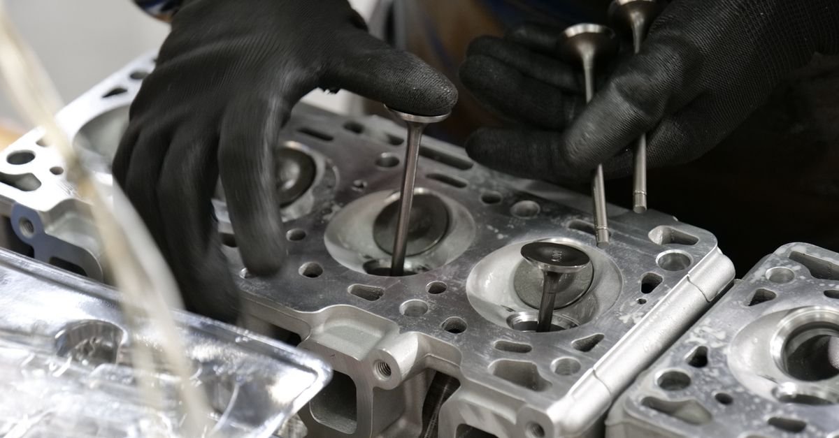 A technician's hands on a stripped cylinder head, where heat-damaged seals show up first