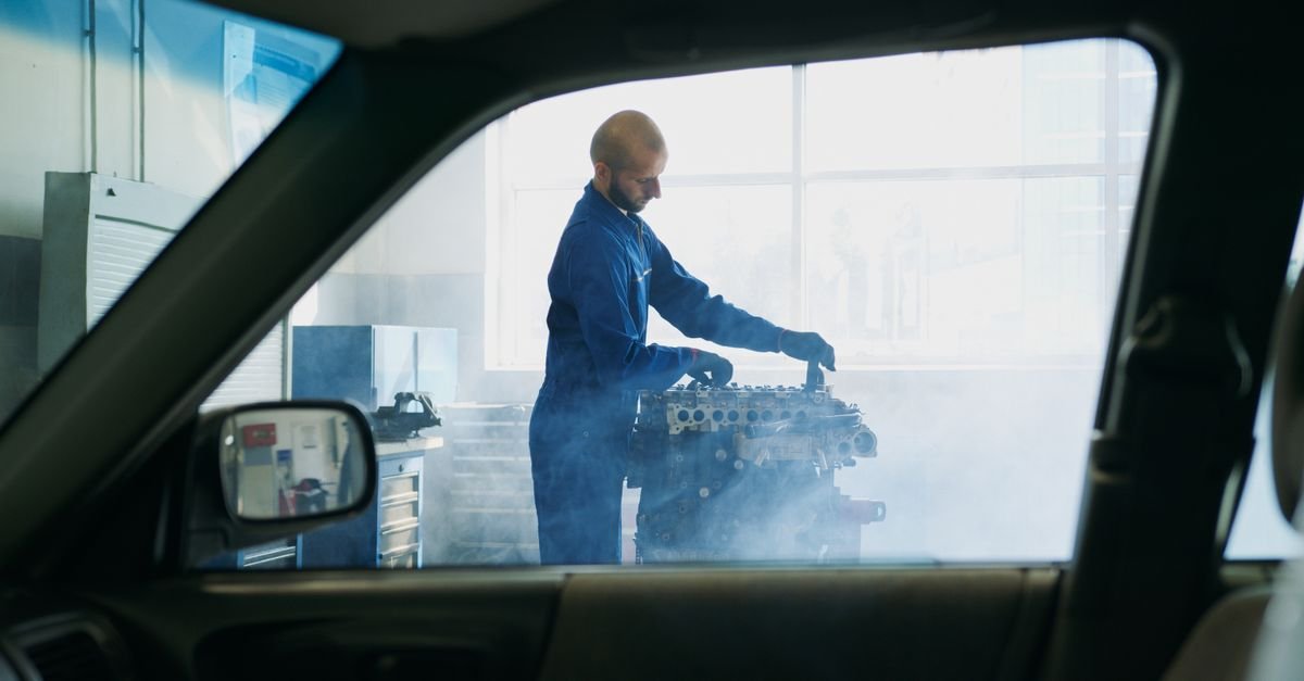 A mechanic checking over a hot engine in a garage with steam still rising from it