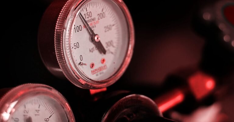Bank of industrial pressure gauges lit in red, needles sitting high on their dials