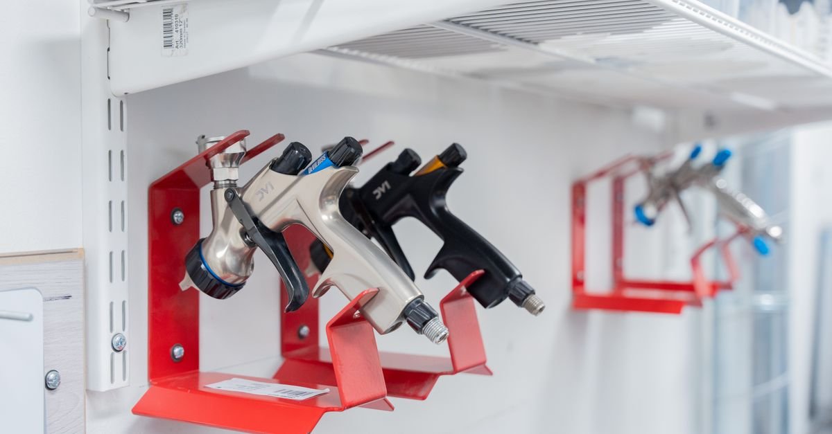 Three spray guns hung on red wall mounts in a workshop, the tip being the first thing to come off a juddering machine