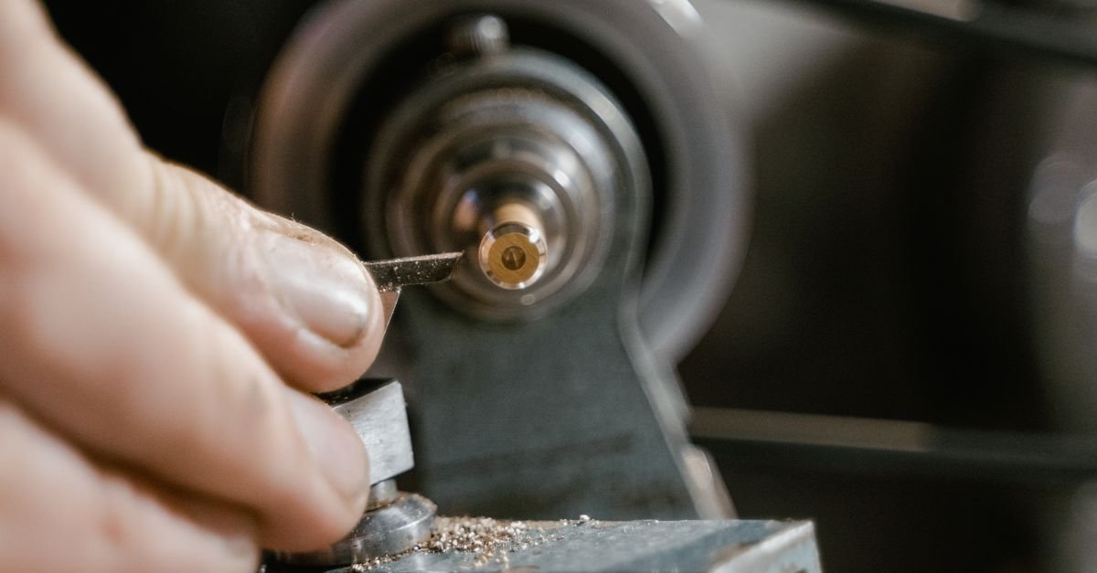 A machinist's hands turning a small metal component on a lathe, the kind of plain soft-steel bar that drive keys are cut from