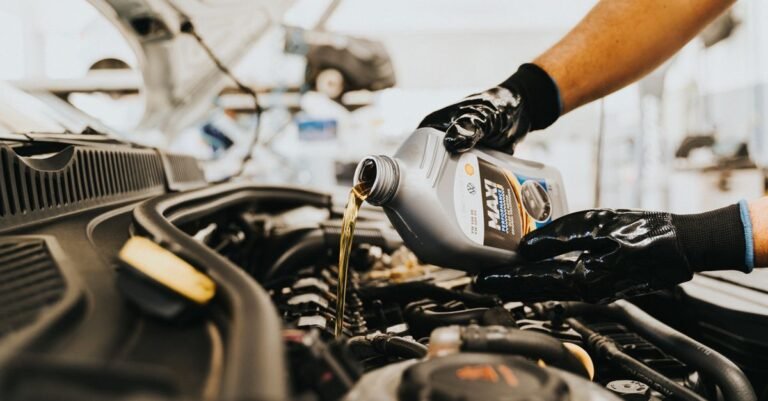 A mechanic in gloves pouring fresh oil from a bottle during a routine oil change