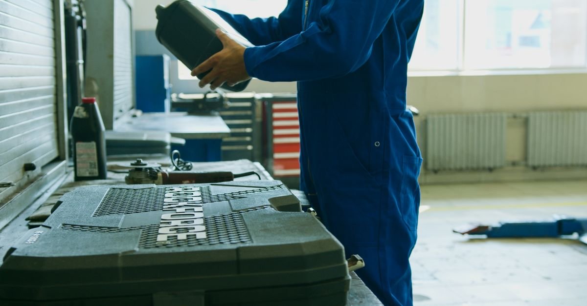 A mechanic in blue overalls holding a bottle of oil in a workshop