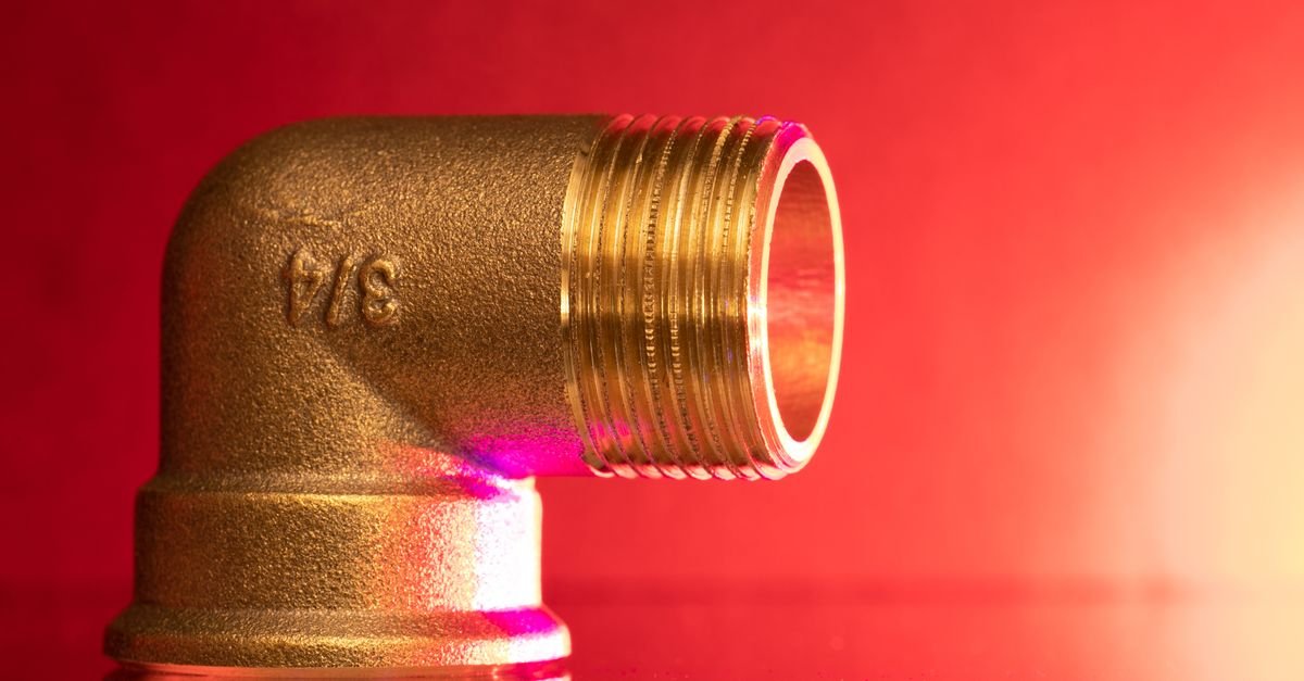 Polished brass elbow fitting photographed in close-up against a red background