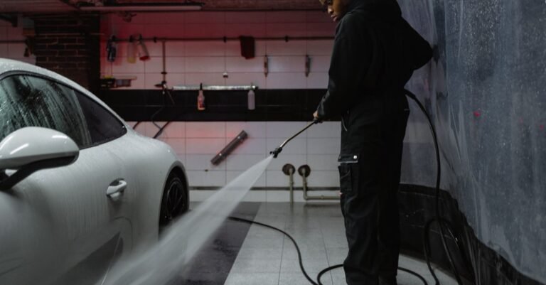 Man cleaning a white car with a pressure washer wand, holding the gun where the quick connect meets the hose
