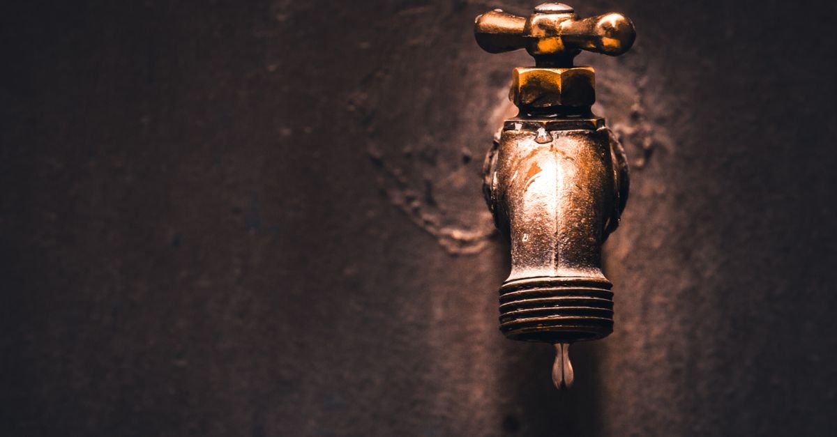 Single water droplet hanging from a brass fitting against a dark background