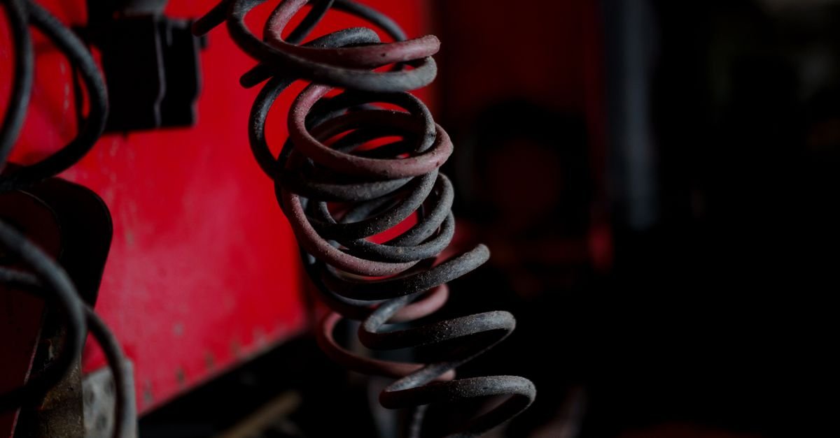 Aged coiled steel springs photographed against a red industrial background, the kind of wound spring that stores every bit of the energy you put into a starter rope