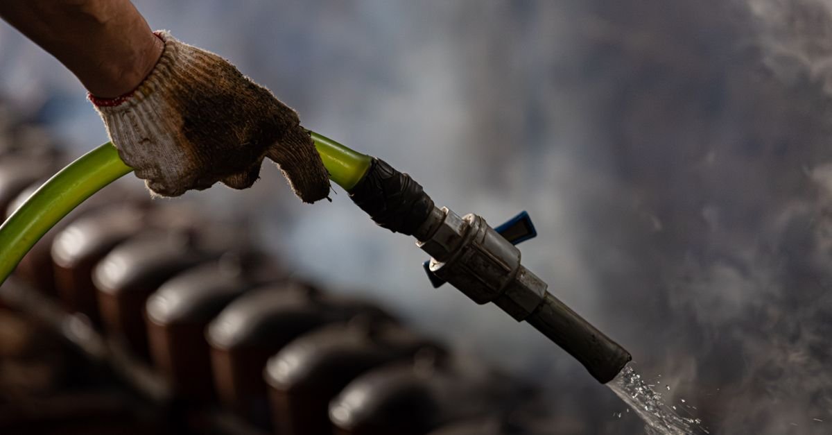 A gloved hand grips an industrial water hose with steam rising in the background