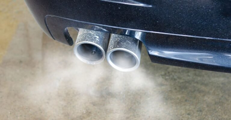 Close-up of an exhaust pipe emitting visible smoke against a dark background