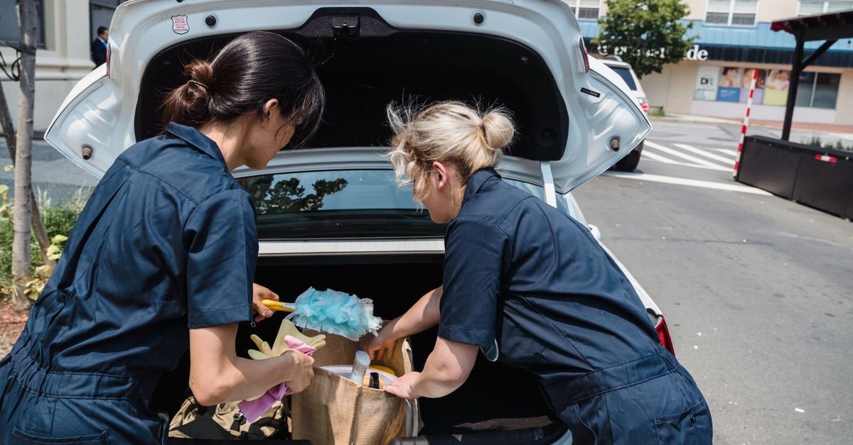 Two people in work uniforms lifting cleaning equipment out of a car boot