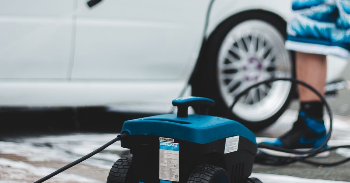 Electric pressure washer unit and coiled hose standing on a paved driveway beside a car