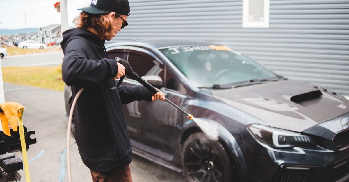 Worker applying detergent with a pressure washer wand held close to a black car