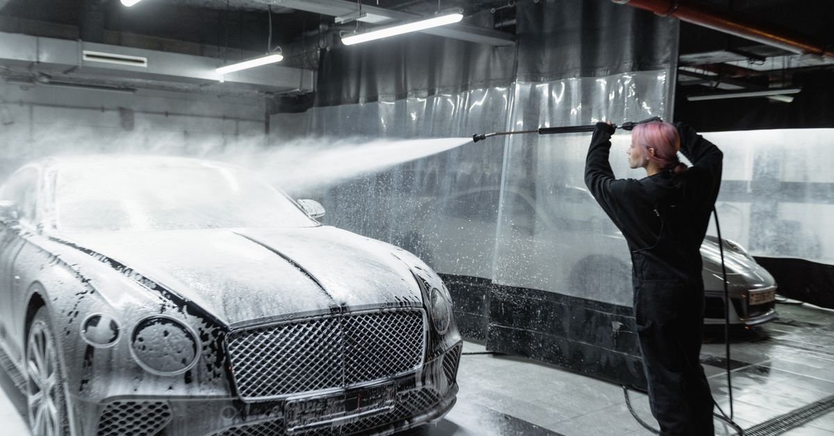 Snow foam being applied to a car with a foam cannon in a wash bay
