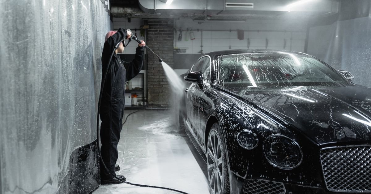 Black car covered in soap and water spray in a garage during a pressure washer wash
