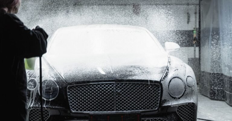Black car coated in detergent foam from a pressure washer soap nozzle in a wash bay
