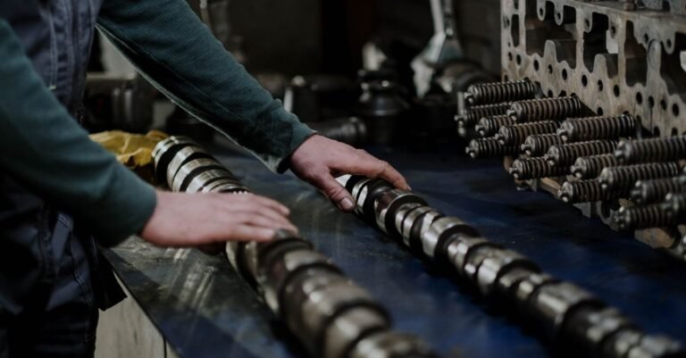 A worker handling camshafts and a cylinder head on a bench in a mechanic's workshop