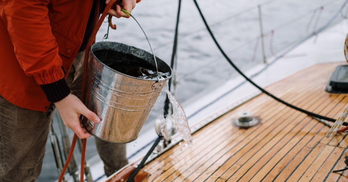 Close-up of a person washing a boat deck with water drawn from a metal bucket, the sort of open container a detergent siphon tube works from