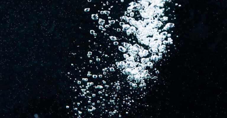 Close-up of air bubbles rising and breaking out through dark water, the air being delivered rather than formed
