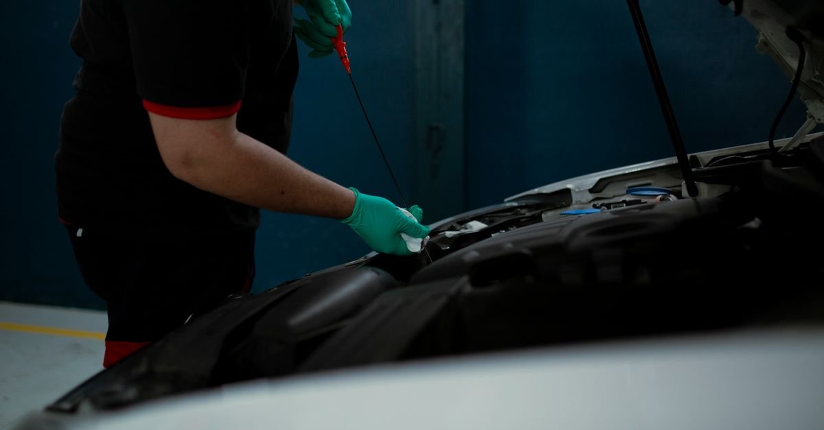 Gloved hands checking an engine oil level with the dipstick