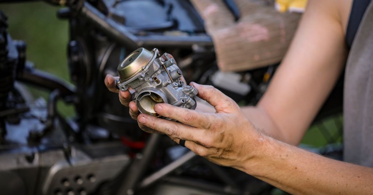Hands holding a small engine carburetor removed for cleaning