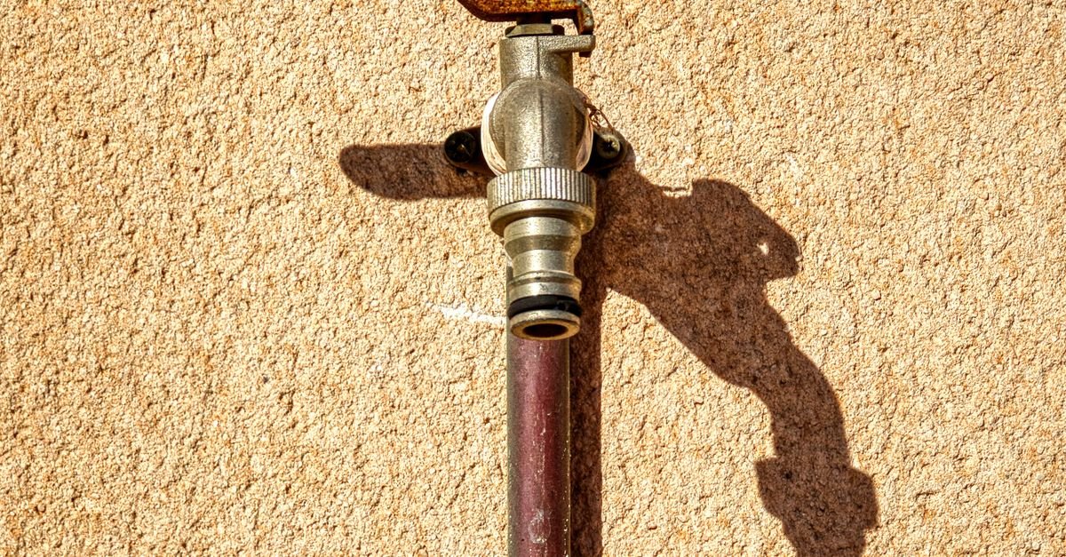 A metal outdoor tap mounted on a textured wall, the supply point where an inlet starvation problem usually begins