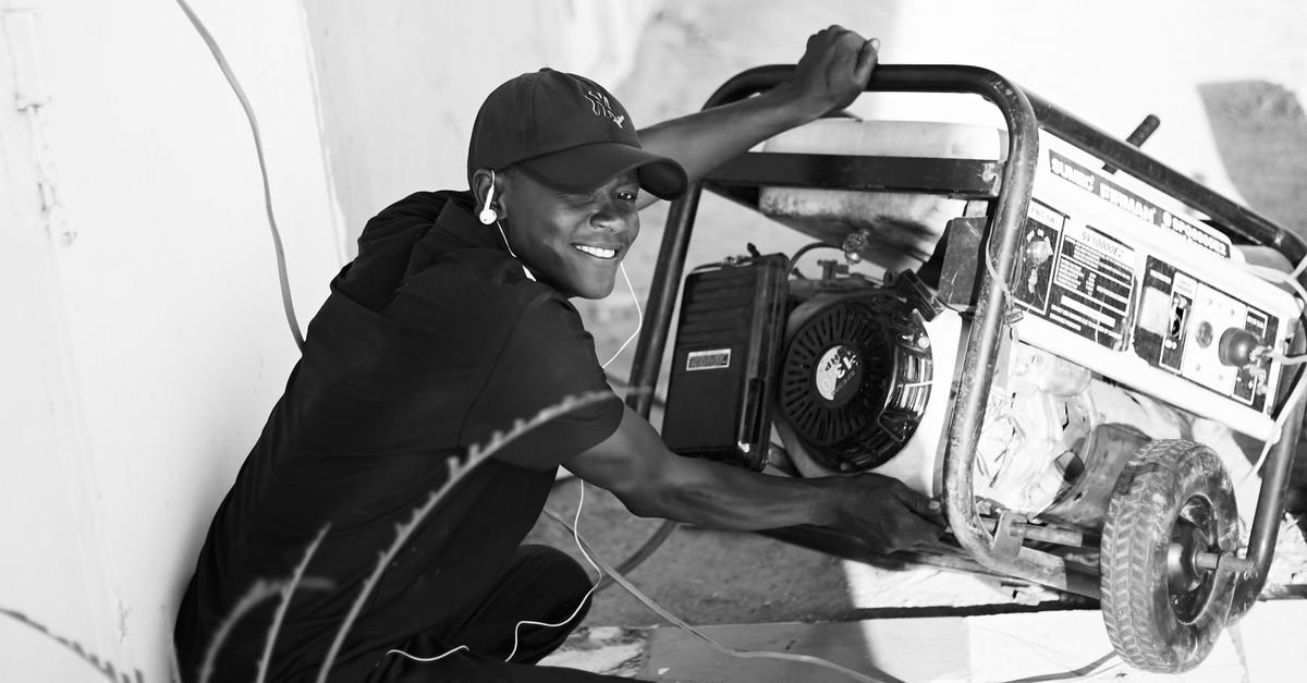 A man operating a small portable gasoline generator outdoors, the same governed engine layout a gas pressure washer uses