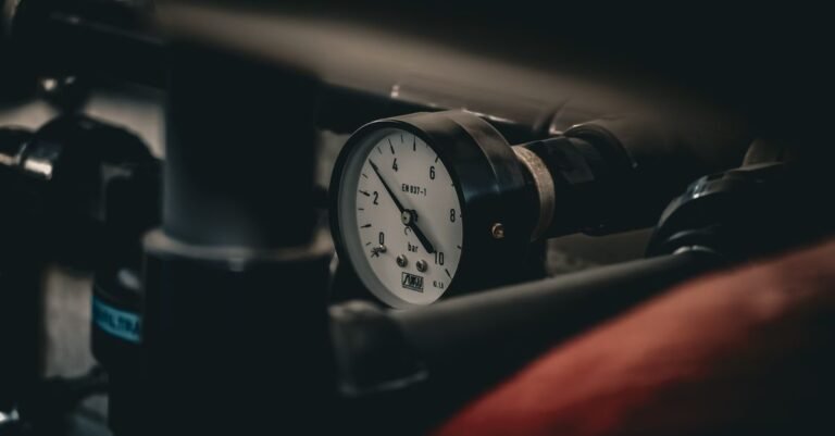 A pressure gauge on an industrial pipe with the needle mid-sweep, the reading a surging pressure washer never settles on