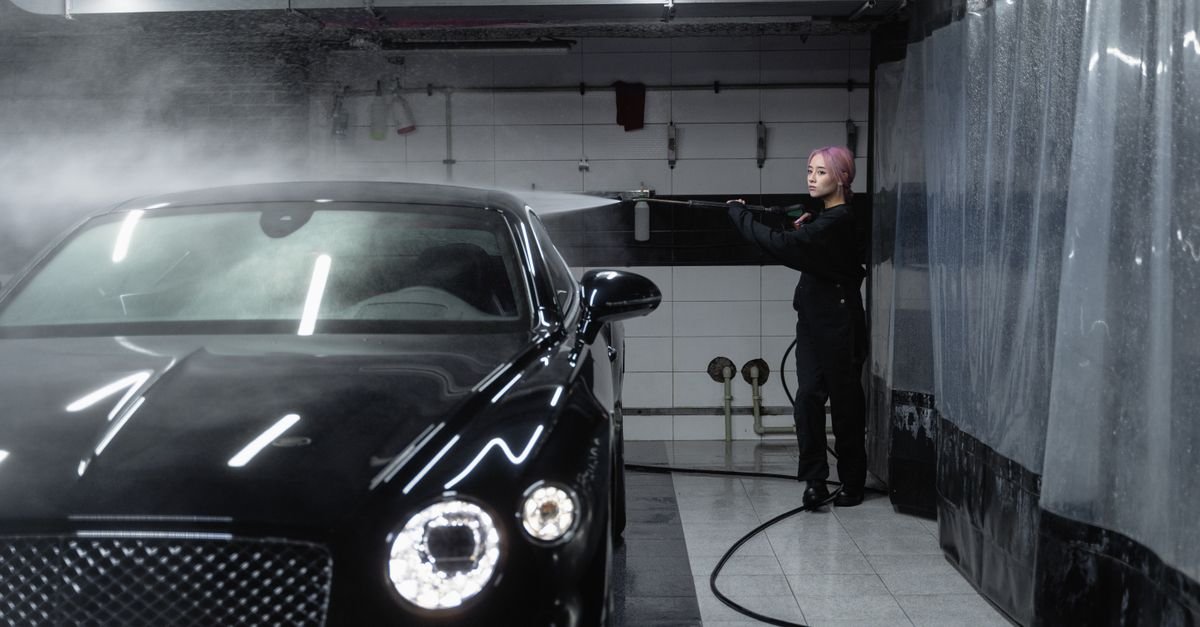 A person washing a car with a pressure washer inside a garage, the trigger held open where a spraying surge shows up