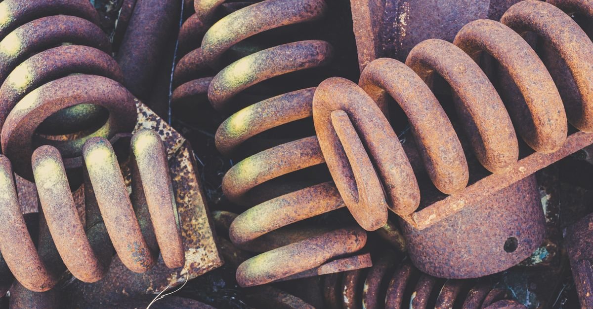 Weathered and rusted coil springs piled in a scrapyard, the same component that returns a trigger lever to its rest position