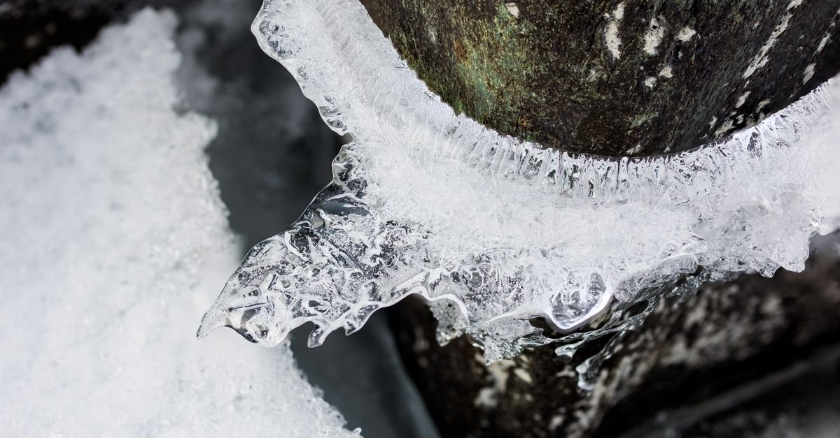 Ice locked around a stone in a frozen river, the way water expands and grips whatever it surrounds