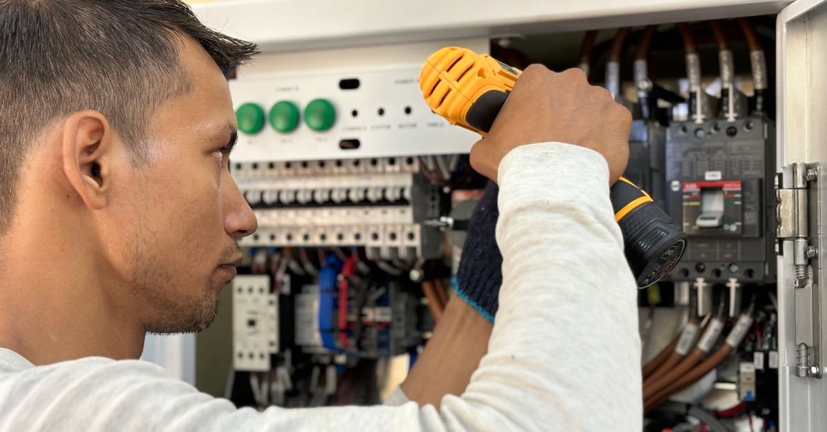 An electrician working inside a residential breaker panel with a power tool